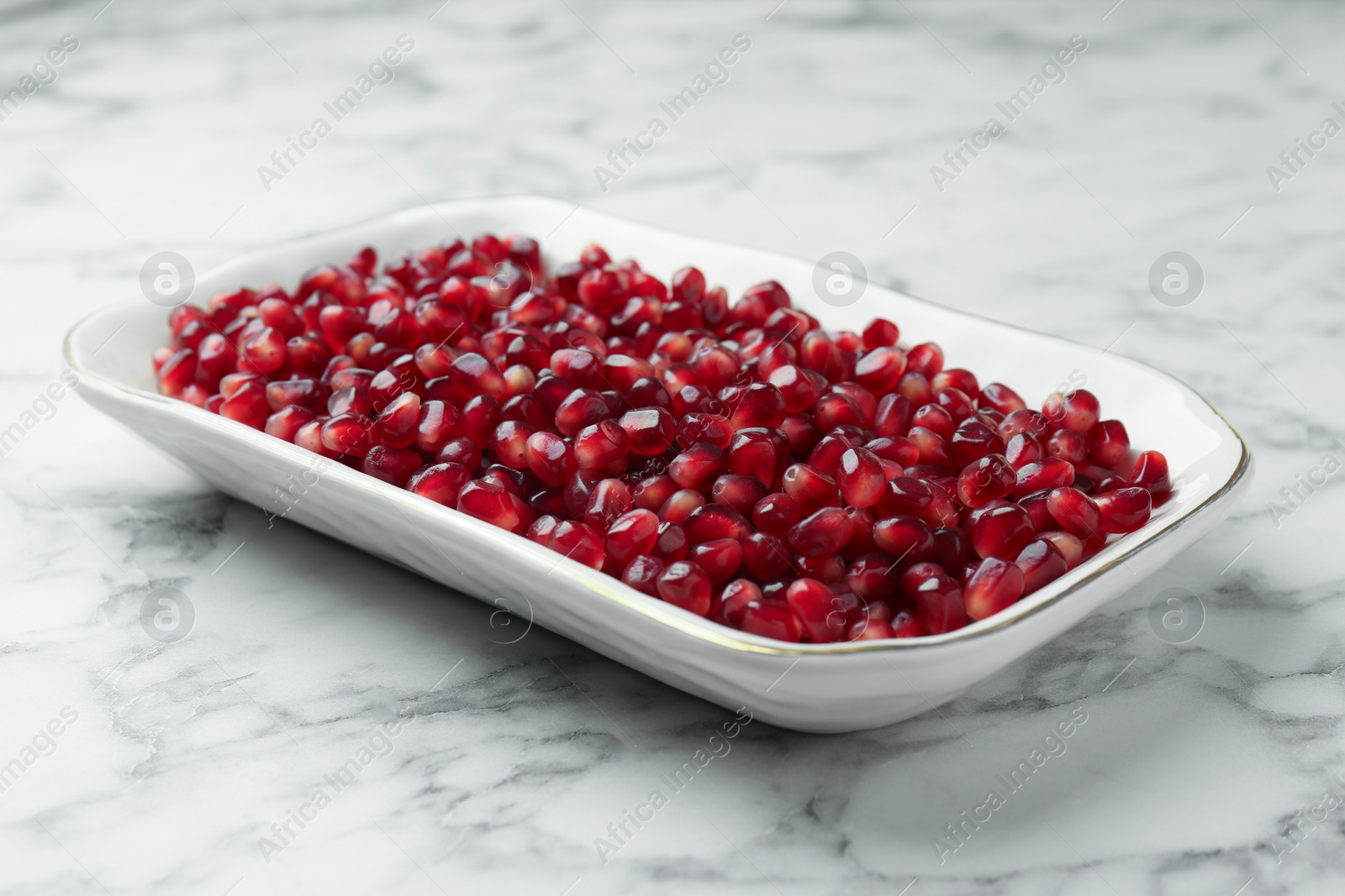 Photo of Ripe juicy pomegranate grains on white marble table