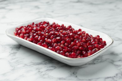 Photo of Ripe juicy pomegranate grains on white marble table