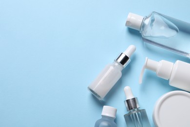 Many different bottles of cosmetic serum on light blue background, flat lay. Space for text