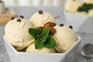 Photo of Delicious vanilla ice cream with mint, hazelnuts and chocolate chips in bowl on table, closeup
