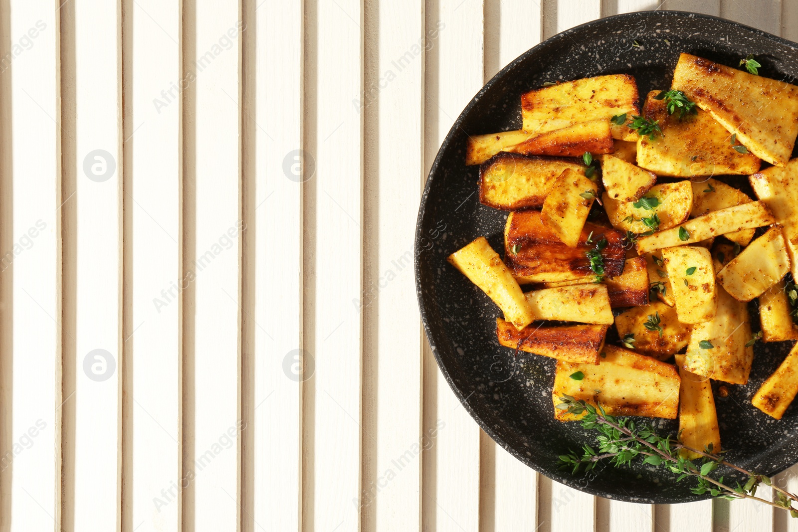 Photo of Delicious parsnips with thyme in frying pan on white wooden table, top view. Space for text