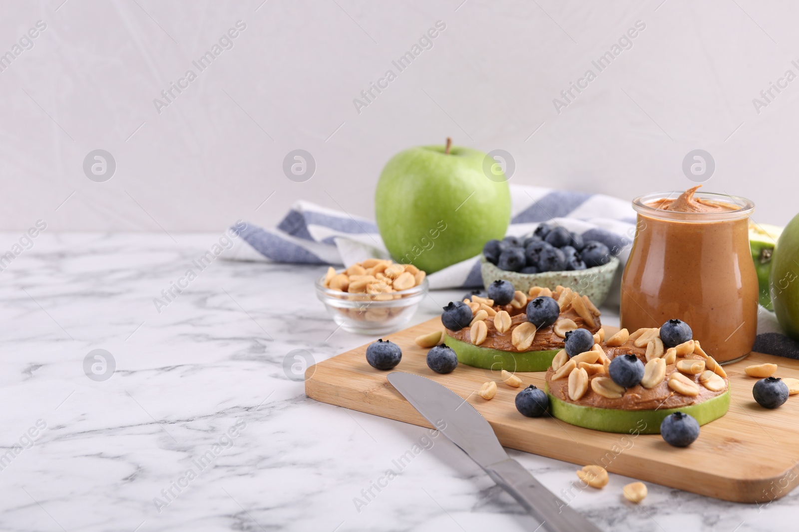 Photo of Fresh green apples with peanut butter, blueberries and nuts on white marble table, space for text