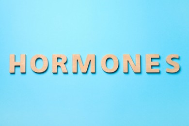 Photo of Word Hormones made of wooden letters on light blue background, flat lay