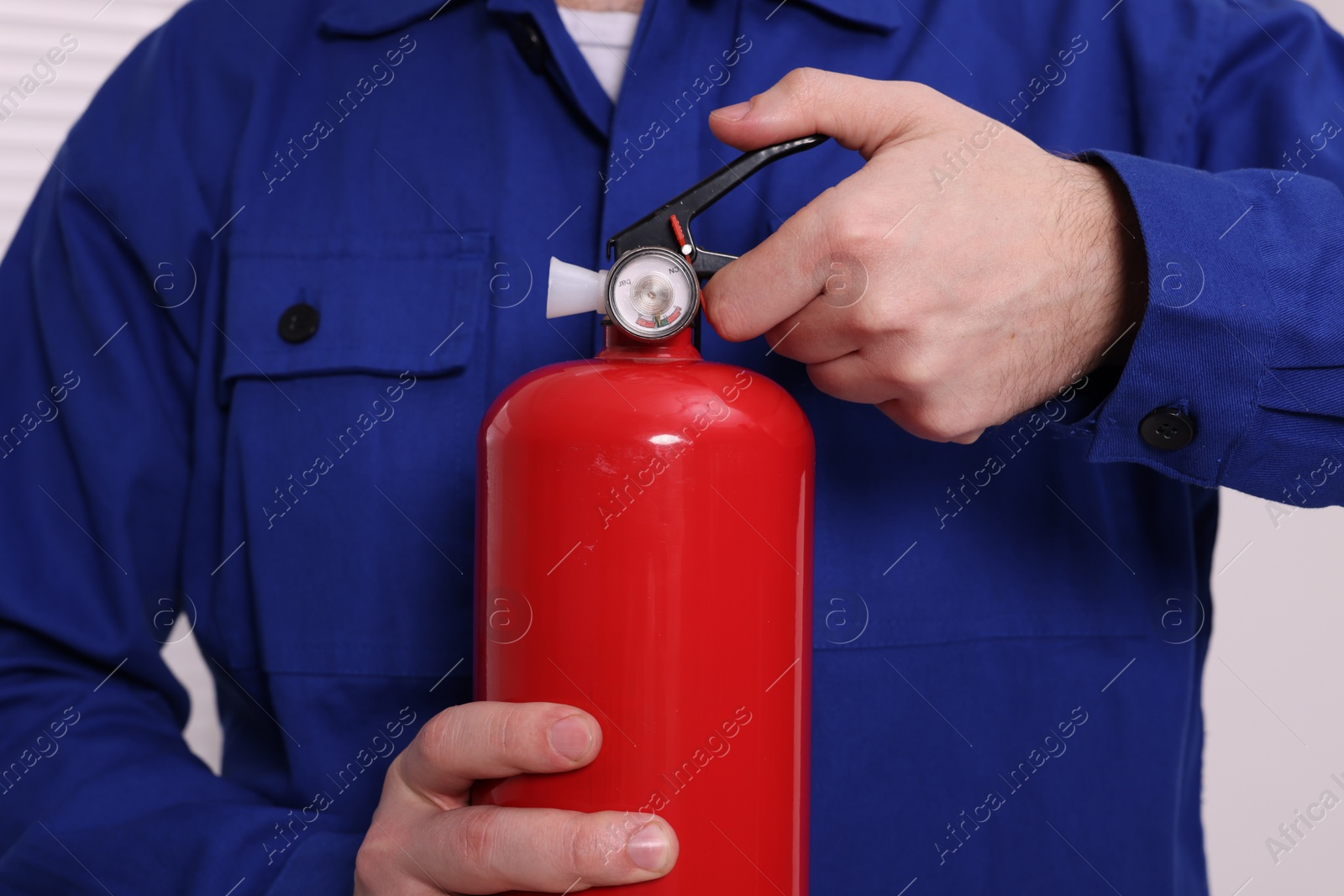 Photo of Man checking quality of fire extinguisher indoors, closeup