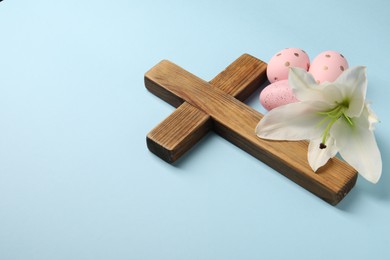 Photo of Wooden cross, painted Easter eggs and lily flower on light blue background, space for text