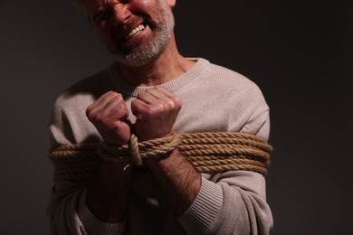 Emotional victim tied with rope on dark background, closeup. Hostage taking