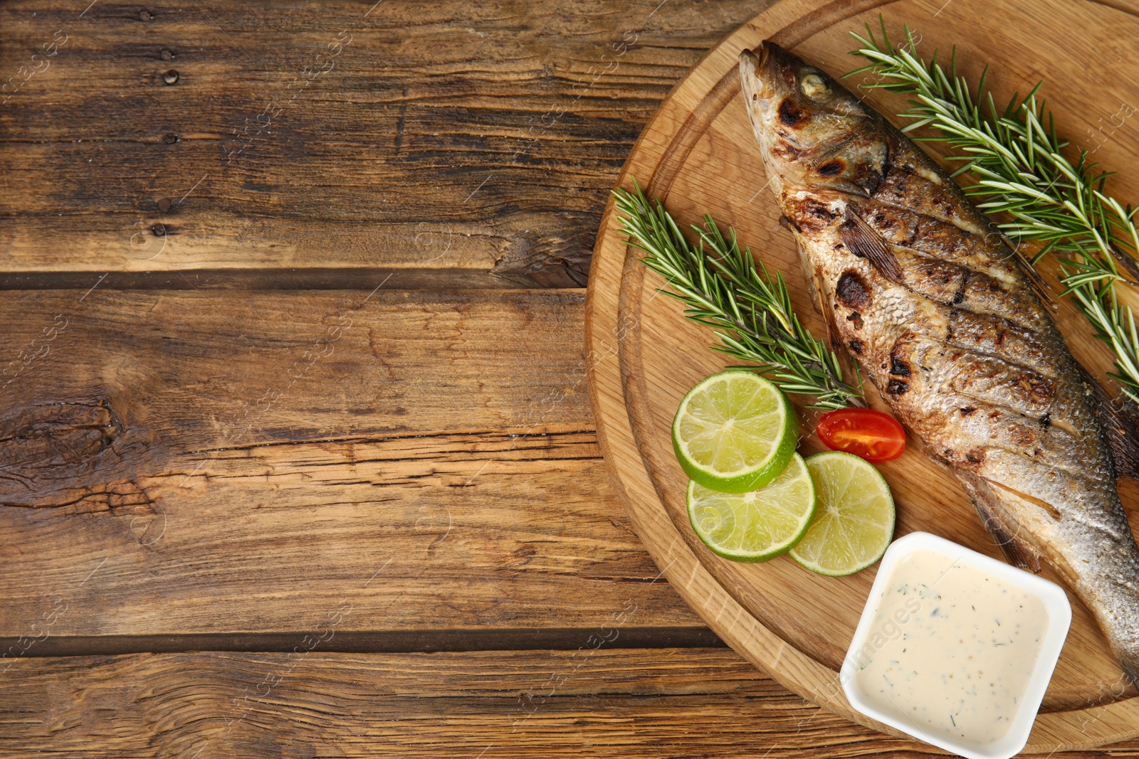 Photo of Delicious grilled fish served on wooden table, top view. Space for text