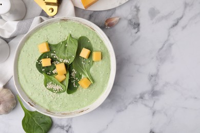 Photo of Delicious spinach cream soup with cheese and sesame seeds in bowl on white marble table, flat lay. Space for text