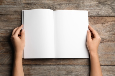 Woman holding brochure with blank pages on wooden background, top view. Mock up for design