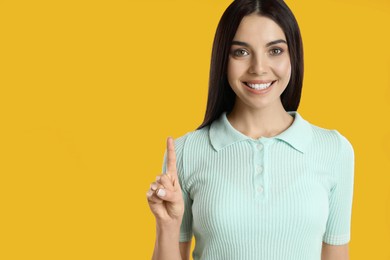 Photo of Woman showing number one with her hand on yellow background, closeup