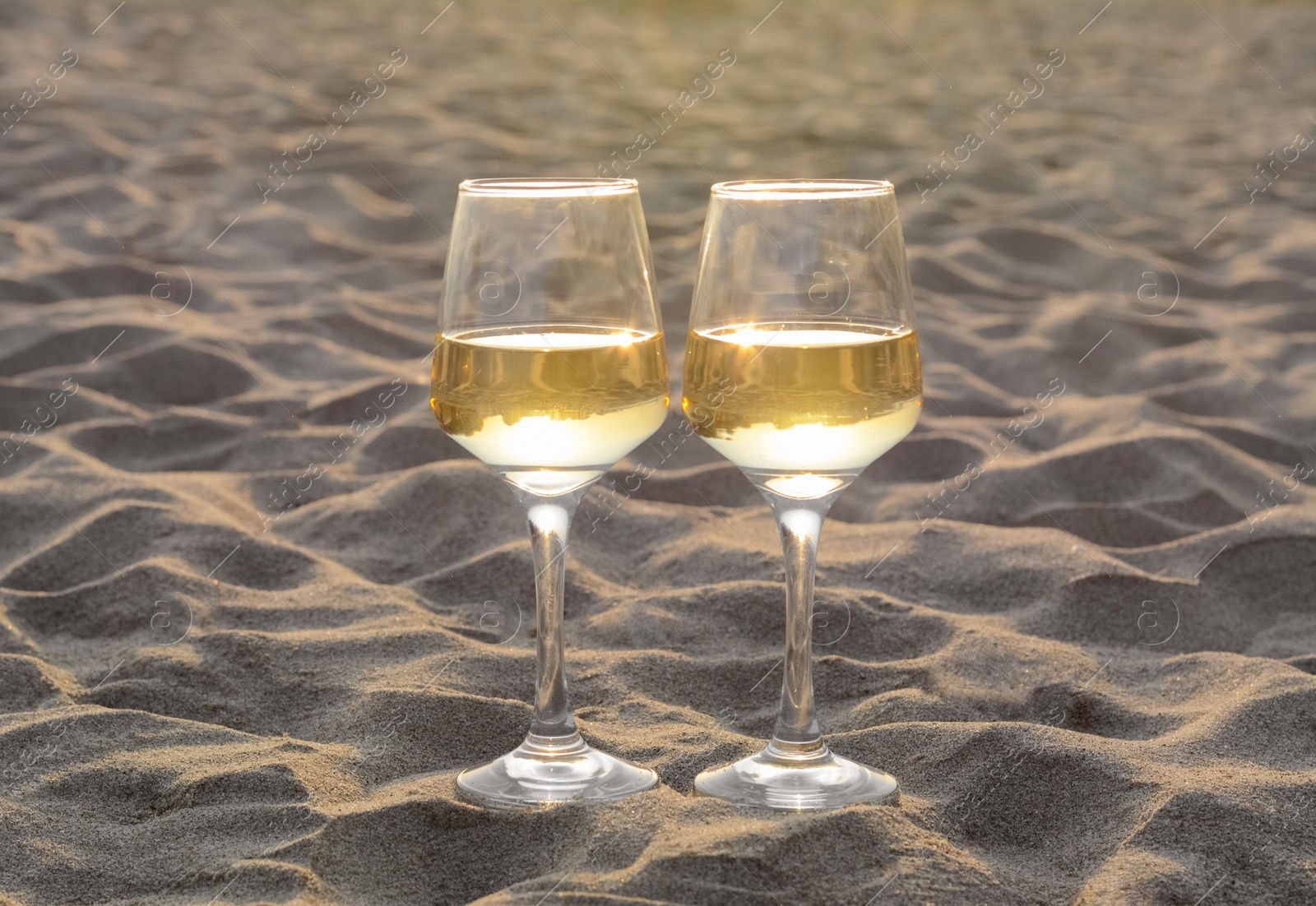 Photo of Glasses of tasty white wine on sand