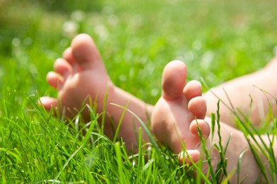 Photo of Child sitting barefoot on green grass outdoors, closeup