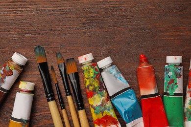 Photo of Tubes with oil paints and brushes on wooden table, flat lay. Space for text