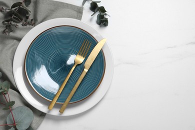 Photo of Stylish setting with cutlery and eucalyptus leaves on white marble table, flat lay. Space for text