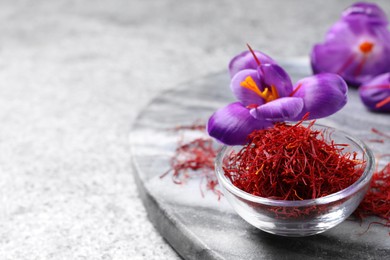 Photo of Dried saffron in bowl and crocus flowers on grey table. Space for text