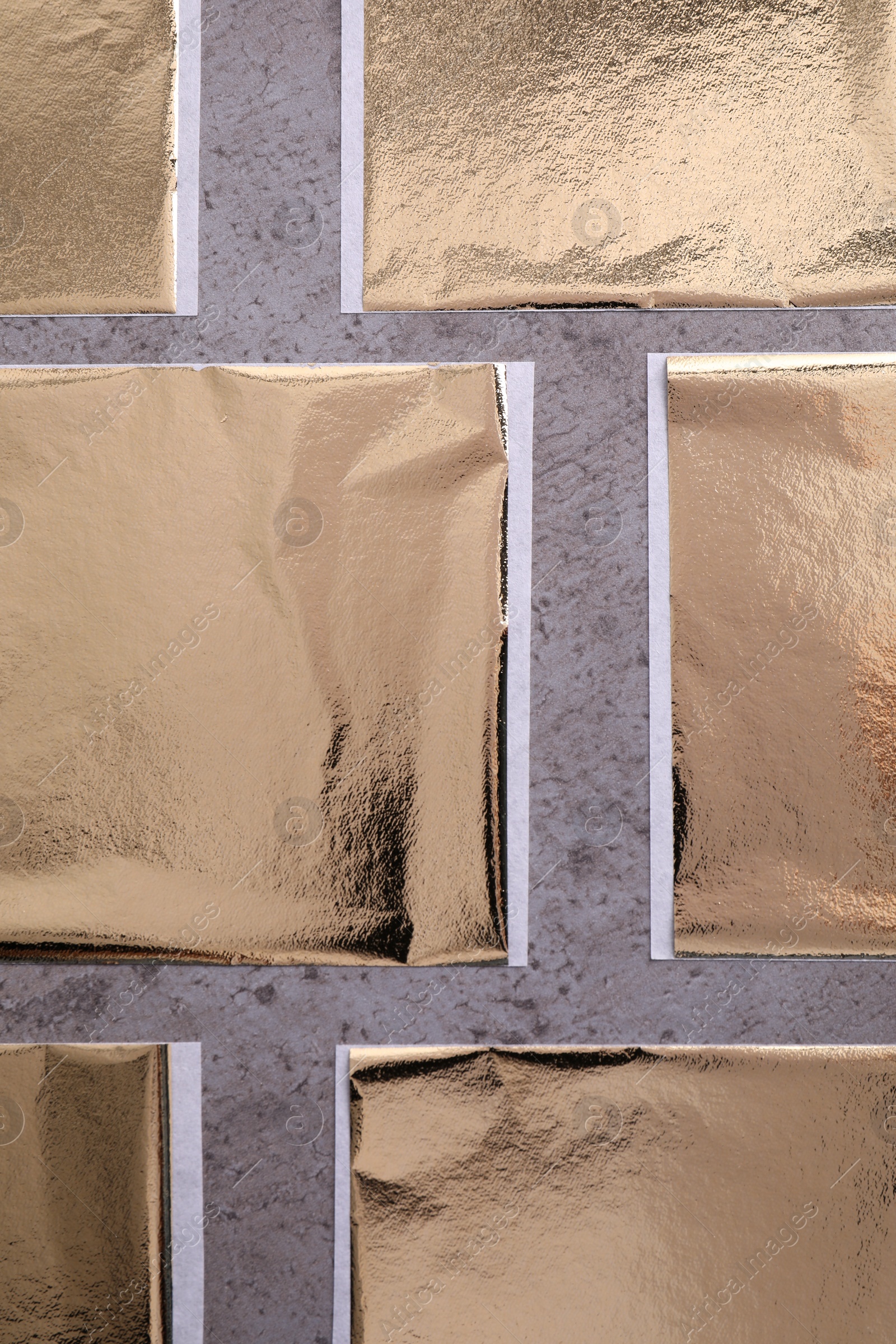 Photo of Many edible gold leaf sheets on grey textured table, flat lay