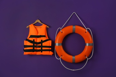 Orange life jacket and lifebuoy on violet background. Rescue equipment