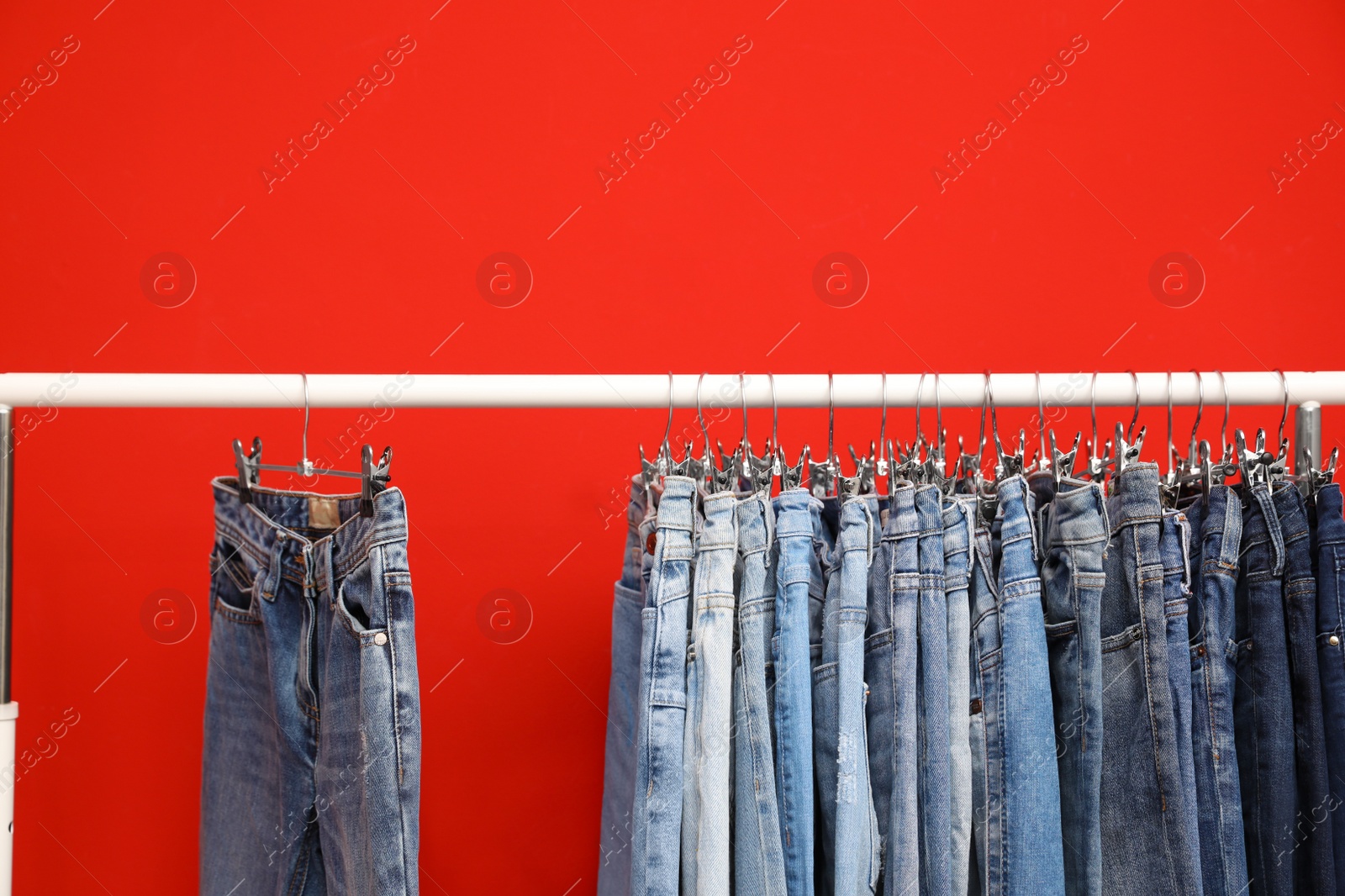 Photo of Rack with stylish jeans on red background