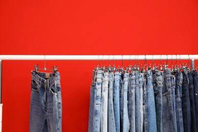 Photo of Rack with stylish jeans on red background