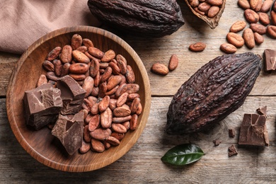 Photo of Flat lay composition with cocoa beans, chocolate pieces and pods on wooden table