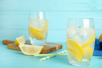 Soda water with lemon slices and ice cubes on light blue wooden table. Space for text