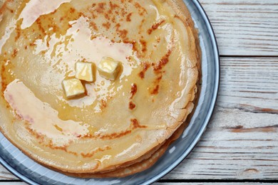 Photo of Delicious crepes with melting butter on white wooden table, top view