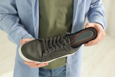 Photo of Man putting orthopedic insole into shoe indoors, closeup