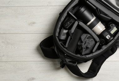 Photo of Backpack with professional photographer's equipment on wooden background, top view. Space for text