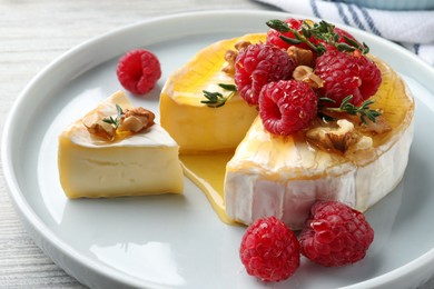 Photo of Brie cheese served with raspberries, walnuts and honey on white wooden table, closeup