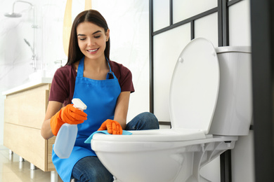Photo of Young woman cleaning toilet bowl in bathroom