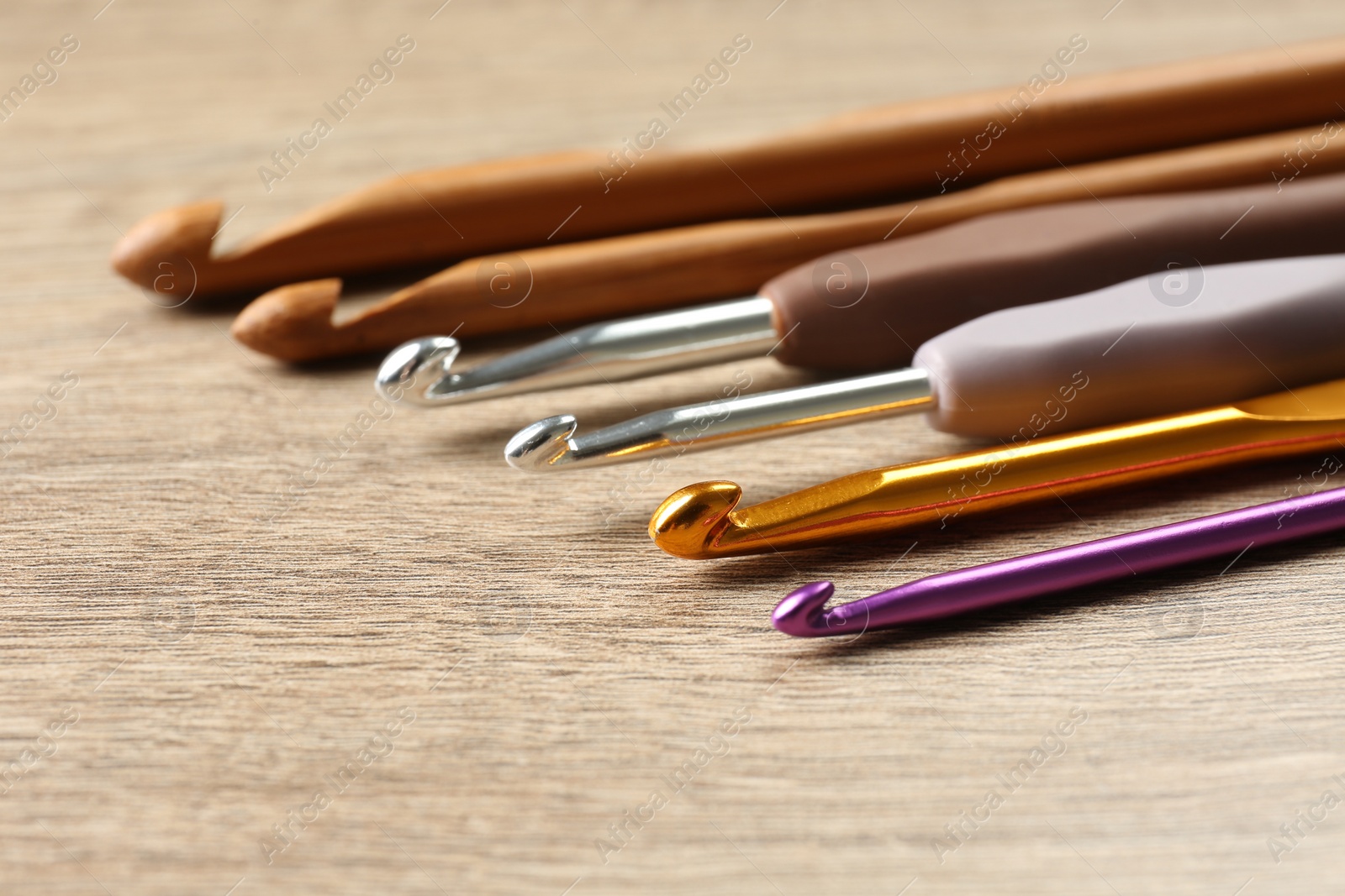 Photo of Many crochet hooks on wooden table, closeup