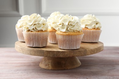 Photo of Tasty cupcakes with vanilla cream on pink wooden table, closeup