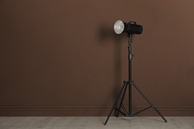 Photo of Studio flash light with reflector on tripod near brown wall in room, space for text. Professional photographer's equipment
