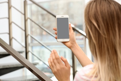 Young woman using video chat on smartphone indoors, closeup. Space for design