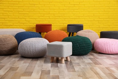 Photo of Many different stylish poufs on floor near yellow brick wall in room