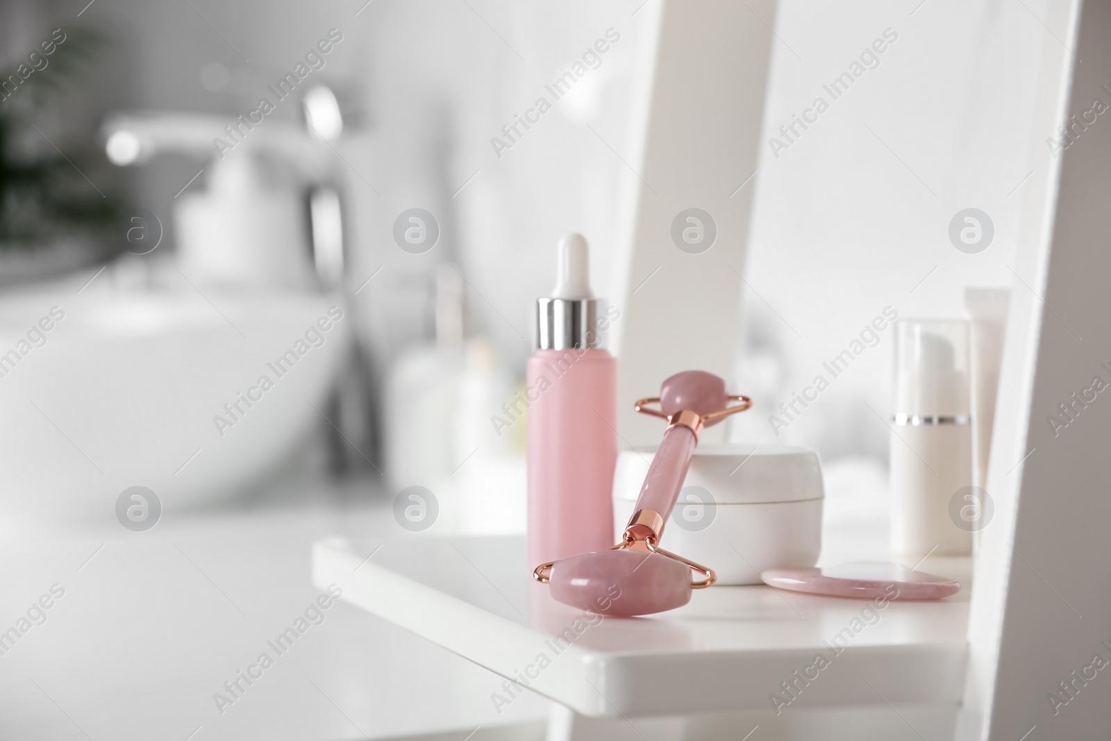 Photo of Natural face roller, gua sha tool and cosmetic products on shelving unit in bathroom. Space for text