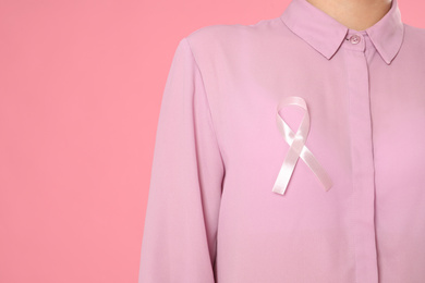 Photo of Closeup view of woman with pink ribbon on color background, space for text. Breast cancer awareness