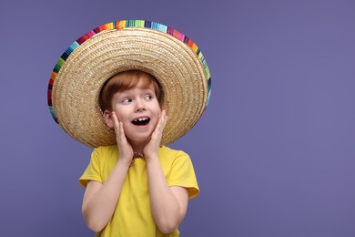 Photo of Surprised boy in Mexican sombrero hat on violet background, space for text