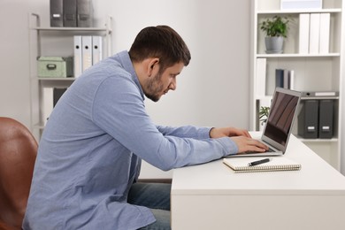 Photo of Man with poor posture working on laptop in office. Symptom of scoliosis