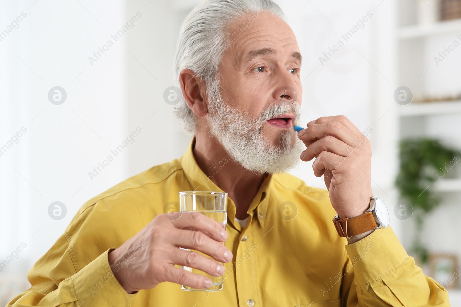 Photo of Senior man with glass of water taking pill indoors