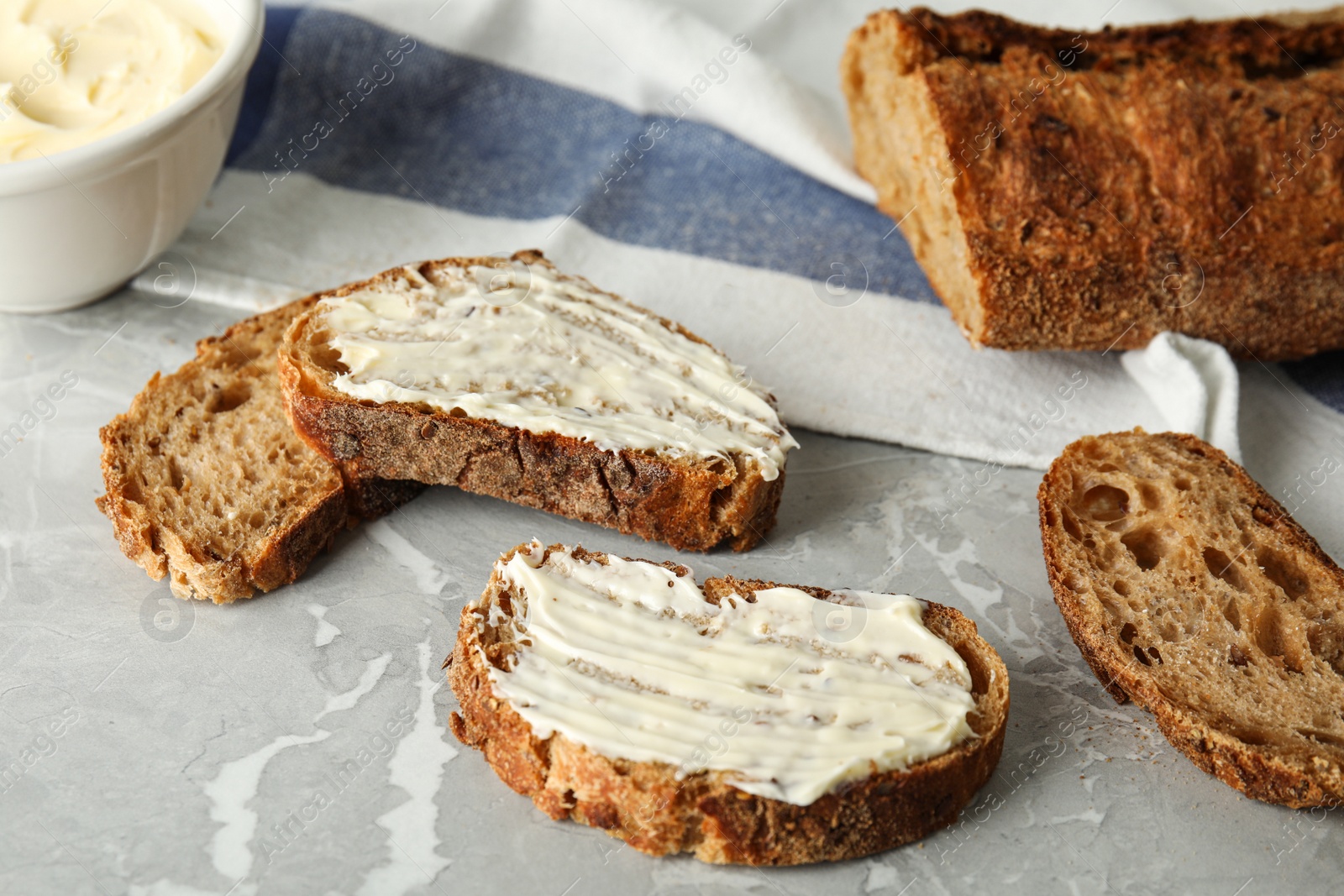 Photo of Slices of tasty bread with butter on grey marble table