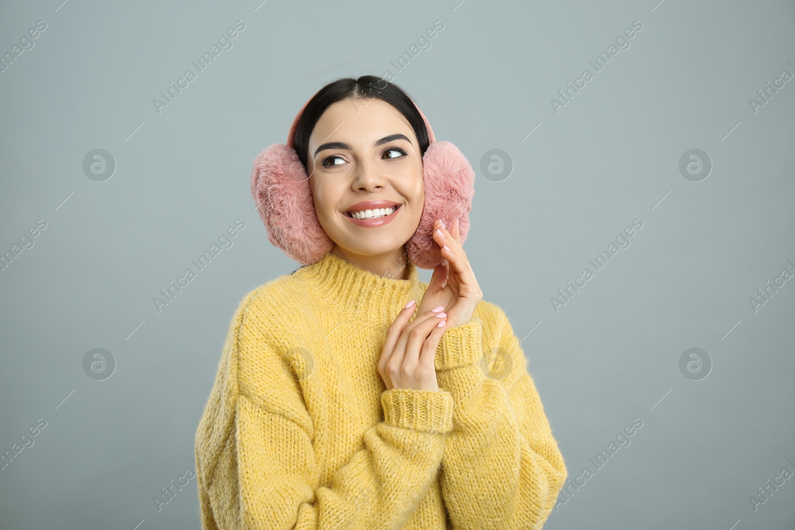 Photo of Beautiful young woman wearing earmuffs on light grey background