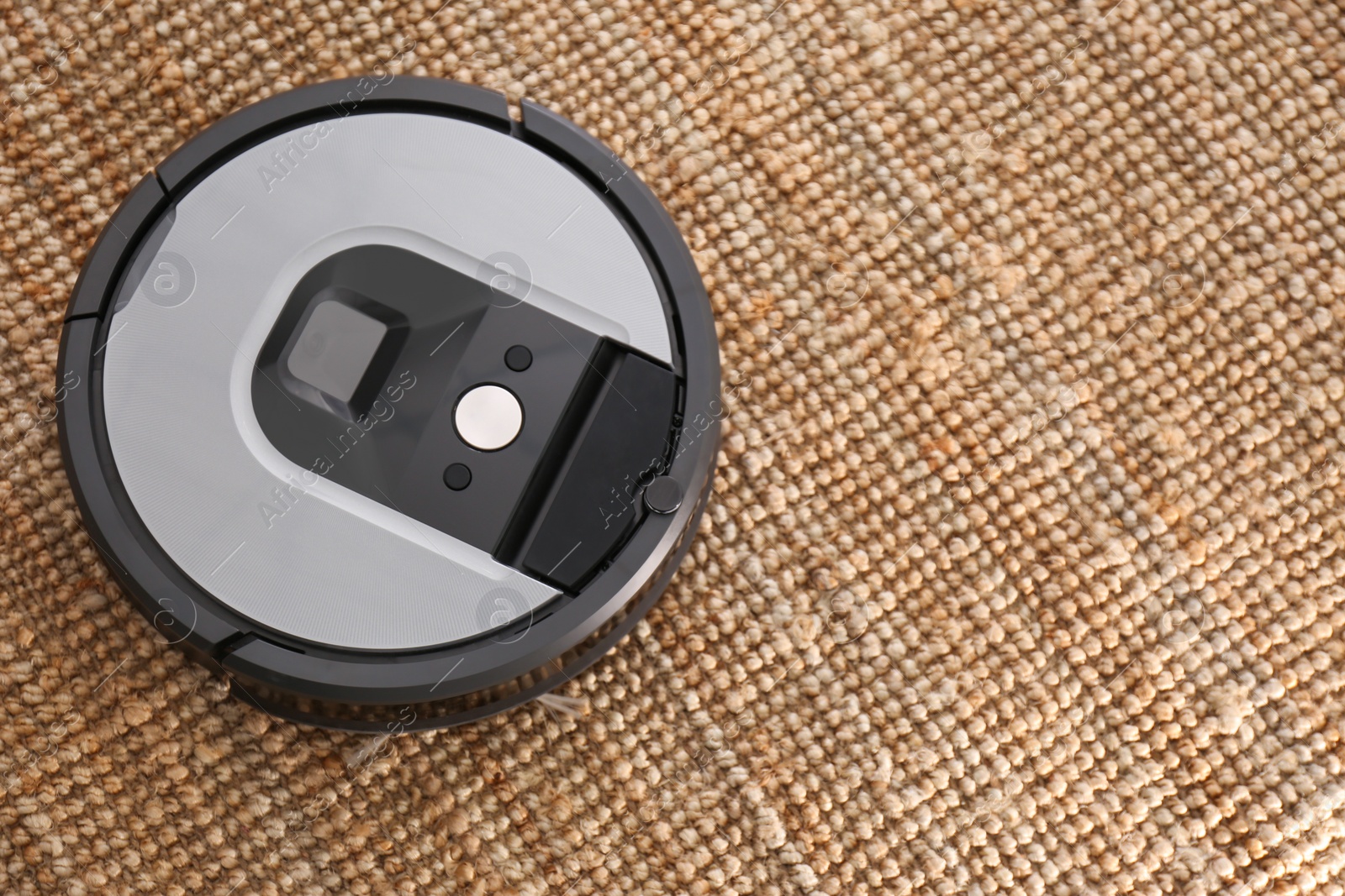 Photo of Modern robotic vacuum cleaner on brown rug, above view. Space for text