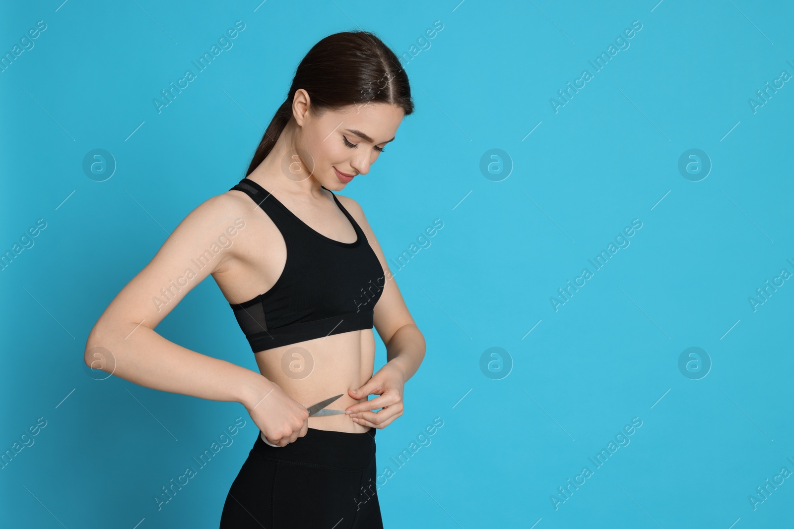 Photo of Slim young woman with scissors on light blue background, space for text. Weight loss surgery