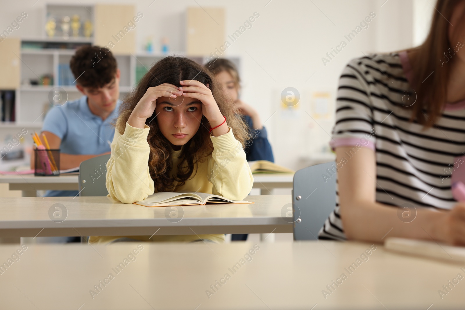 Photo of Teen problems. Lonely girl sitting separately from other students in classroom