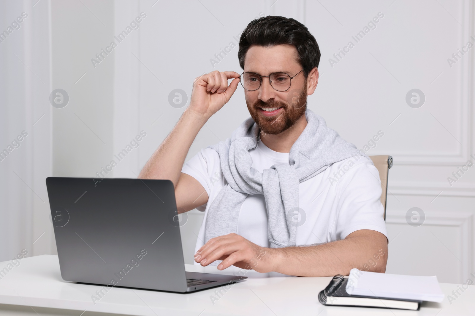 Photo of Man using laptop at white table indoors