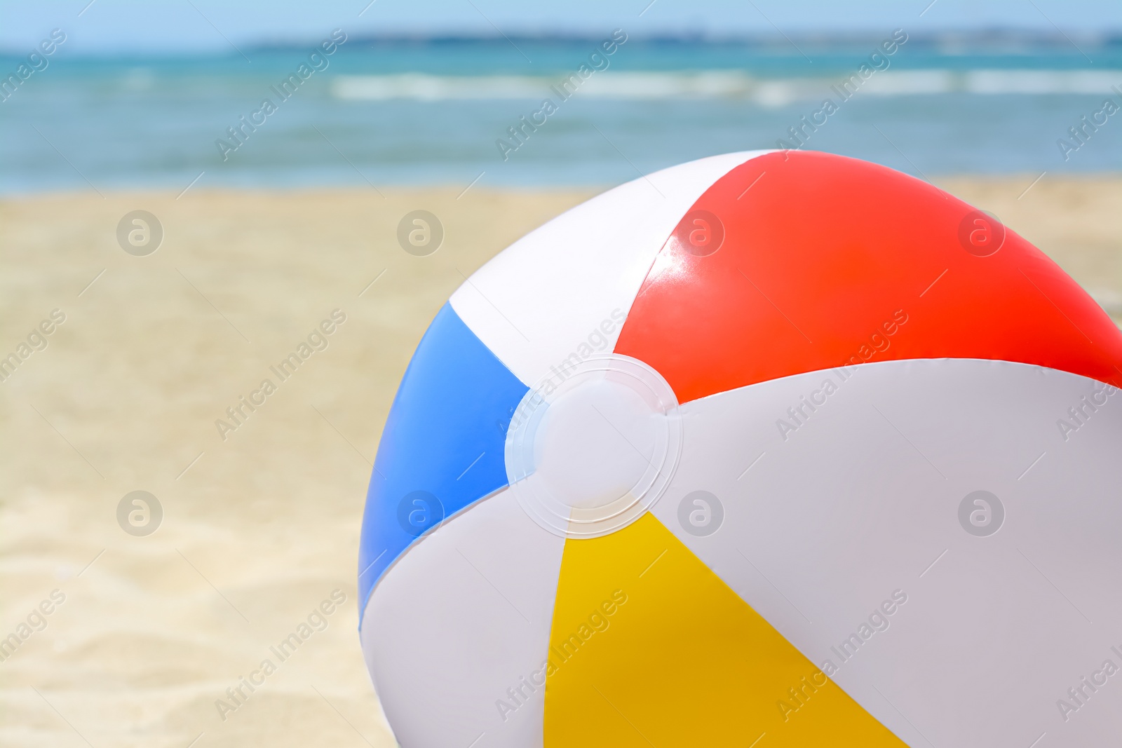 Photo of Colorful beach ball on sand near sea, closeup