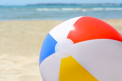 Photo of Colorful beach ball on sand near sea, closeup