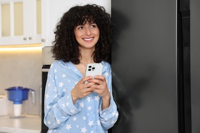 Photo of Beautiful young woman in stylish pyjama with smartphone in kitchen