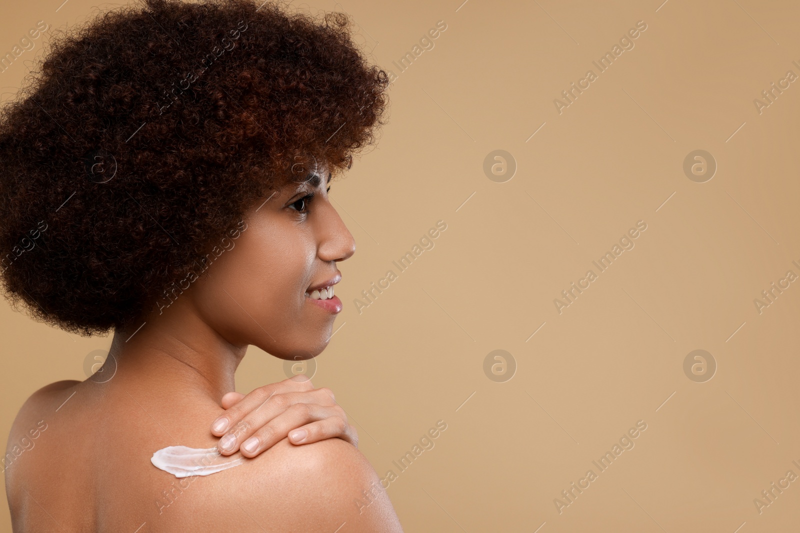 Photo of Beautiful young woman applying body cream onto back on beige background, space for text